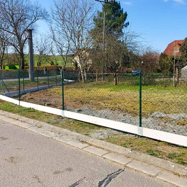 Betonové podhrabové desky pod zeleným čtyřhranným pletivem u silnice, realizace v Býšti 2026